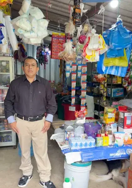 Hombre atendiendo un pequeño negocio con productos en estantes.